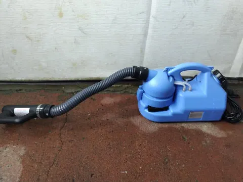 Blue handheld fogging sprayer with a flexible grey hose and black handle on a red floor